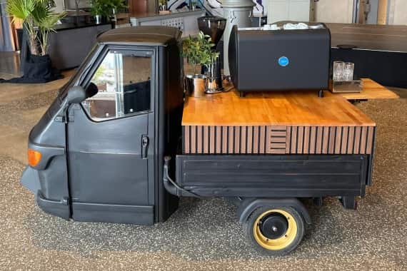 Die schwarze Piaggio Ape, die Markus Grein als mobile Kaffee-Bar für Events nutzt, steht in einer Würzburger Eventlocation.