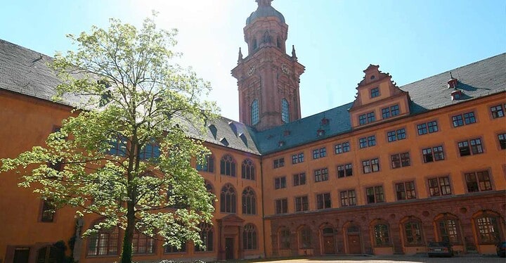 Innenhof der Eventlocation der Neubaukirche in Würzburg mit Blick auf den Kirchturm bei Sonnenschein und blauem Himmel.