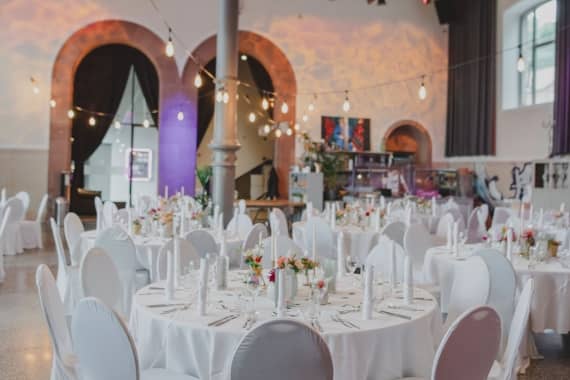 Festlich dekorierte runde Hochzeitstische mit weißen Hussen und Hochzeitscatering in der Bürgerbräu Würzburg.