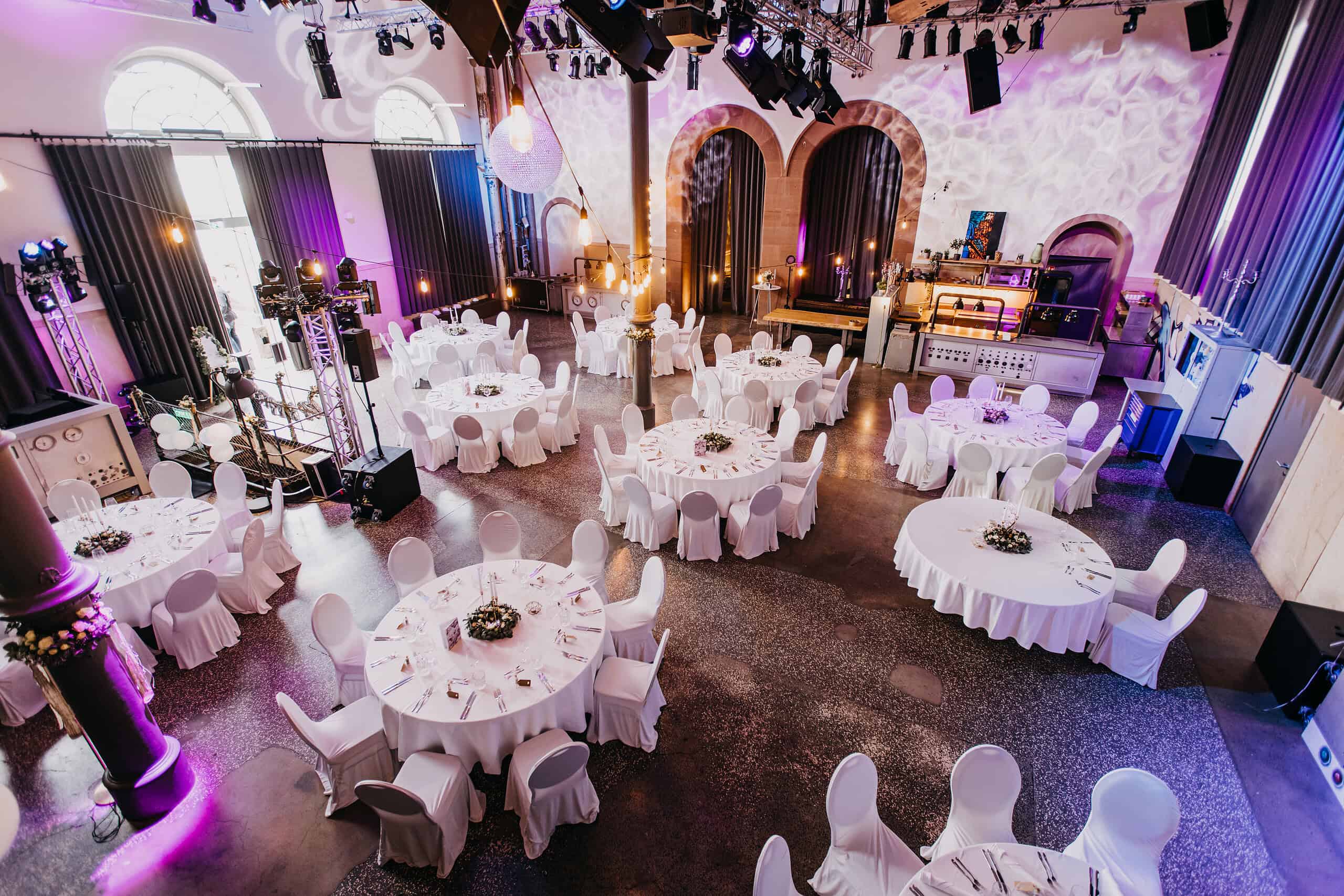 Hochzeitslocation in Würzburg Maschinenhaus Innenansicht mit mehreren runden Tischen für das Hochzeitsessen vorbereitet