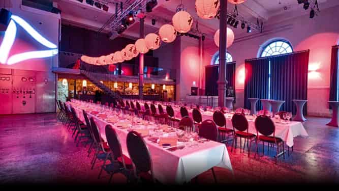 Würzburger Eventlocation Maschinenhaus Bürgerbräu mit zwei Dinnertafeln und Lichtdekoration für eine Abendveranstaltung.