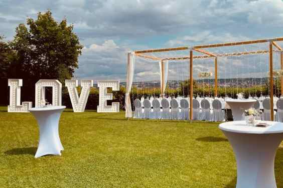 Outdoor-Hochzeitslocation über Würzburg auf Rasen mit LOVE-Schriftzug als Dekoration, Hochzeitstafel und Cocktailtischen.