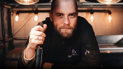 Ein Koch von Markus Grein Catering schaut in die Kamera und hält ein Messer mit der Spitze nach unten in der Hand.