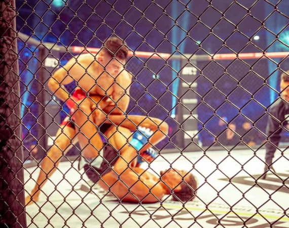 Kampfszene zweier Kämpfer mit Körperkontakt und einer der beiden wird auf den Boden gedrückt bei der Mix Fight Championship