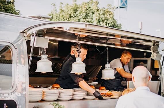 Köche servieren den Gästen bei einem Open-Air-Event Burger aus dem Airstream Foodtruck beim Streetfood-Catering in Frankfurt.