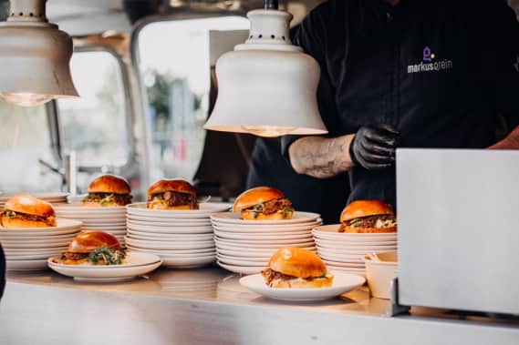 Mehrere Burger liegen servierbereit beim Foodtruck Catering auf der Theke vom Airstream von Markus Grein Catering.