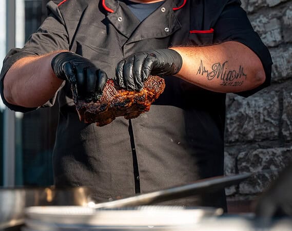 Grill-Caterer hält ein Stück frisch gegrilltes Fleisch beim BBQ-Catering in Würzburg