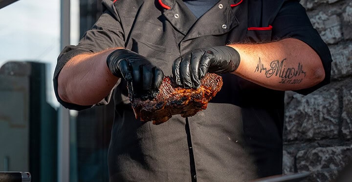 Grill-Caterer hält ein Stück frisch gegrilltes Fleisch beim BBQ-Catering in Würzburg
