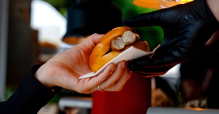Gast erhält ein frisch Bratwurst im Brötchen beim Streetfood Catering von Markus Grein