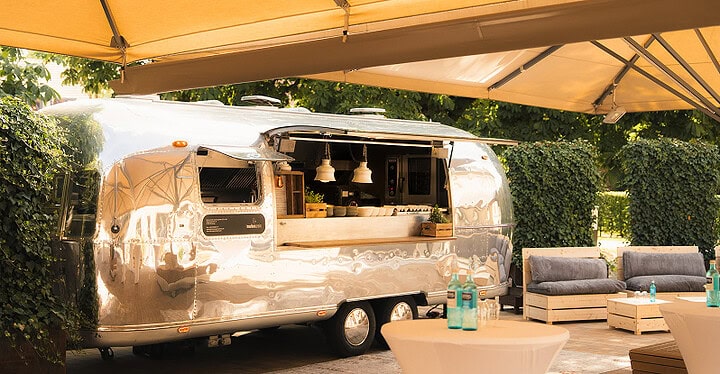 Silberner Airstream Foodtruck mit Markise und Lounge im Garten als Catering für eine Hochzeit