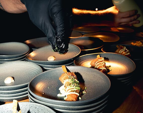 Koch garniert einen gebackenen Spieß mit Kräutern zwischen gestapelten Tellern bei der Gastro Premium Night in Frankfurt