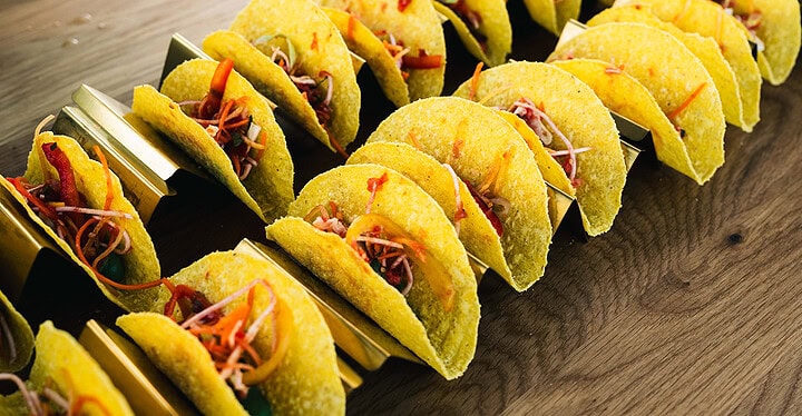 Reihe kleiner gefüllter Mini Tacos auf einem Holzbrett als herzhafte Häppchen zum Sektempfang