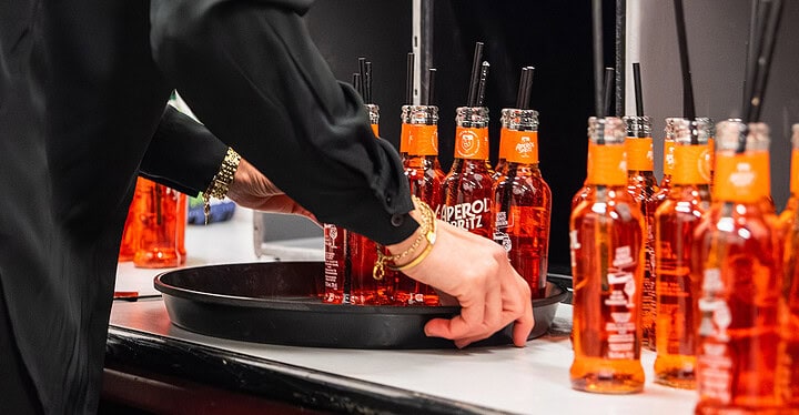 Servicekraft richtet Aperol Spritz Flaschen auf einem Tablett für den Sektempfang einer Hochzeit an