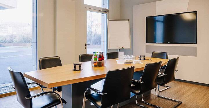 Kleiner Meetingraum des Novum Conference & Events mit Besprechungstisch mit Getränken, Bildschirm, Flipchart.