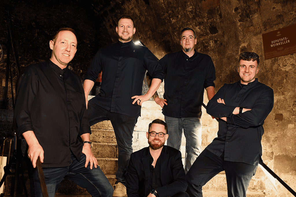 Fünfköpfiges Catering-Team von Markus Grein posiert gemeinsam auf einer Treppe.