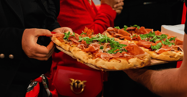 Ein Gast nimmt sich ein Stück Pizza beim Flying-Buffet bei einem Messestand.