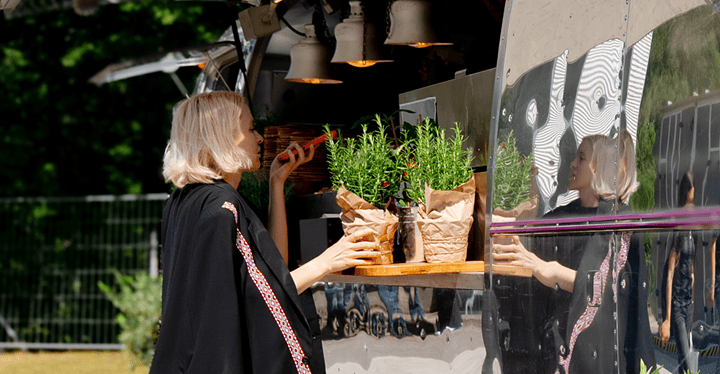 Frau steht auf einem Messegelände vor einem Foodtruck und bestellt eine Speise.