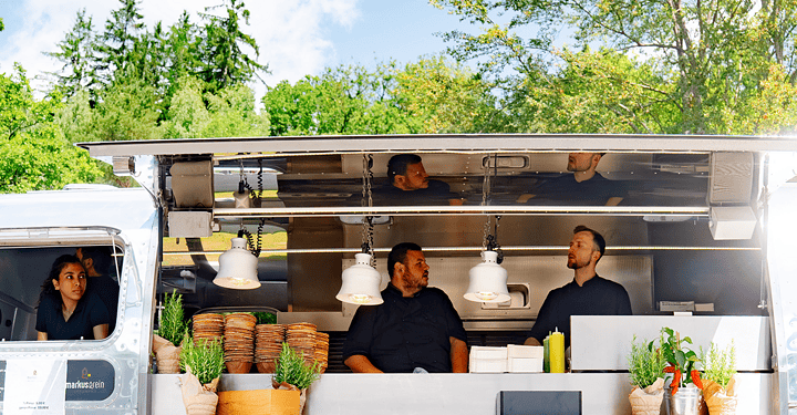 Kochteam bereitet im Airstream-Truck Speisen für das Messe-Catering vor.