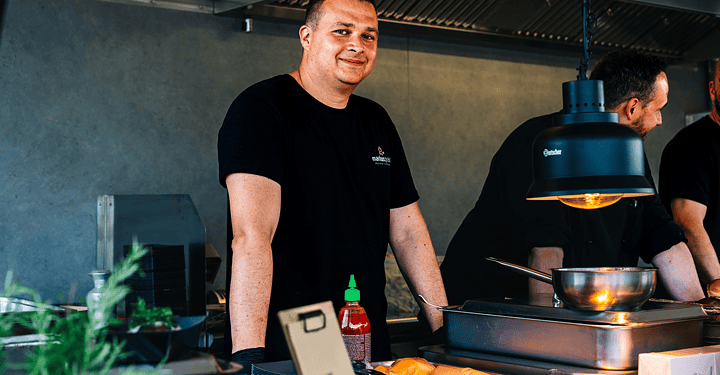 Mitarbeiter steht lächelnd an einer Kochstation mit Wok und Sriracha-Sauce.