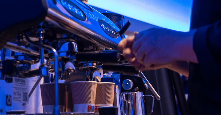 Stand mit einem Barista der Milch an einer Espressomaschine für frisch zubereiteten Kaffee schäumt.