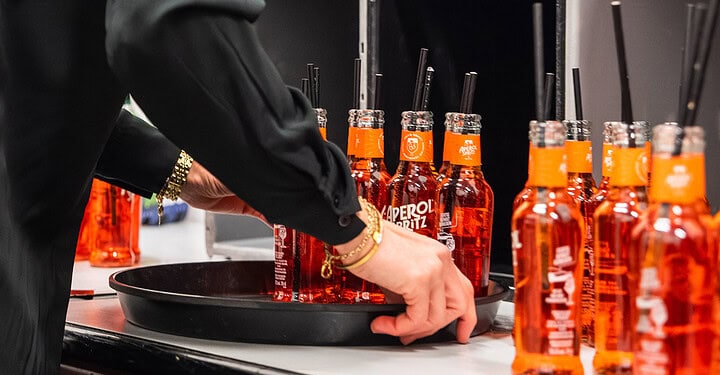 Aperol-Flaschen mit Strohhalmen werden auf einem Tablett für die Messe-Standparty vorbereitet.