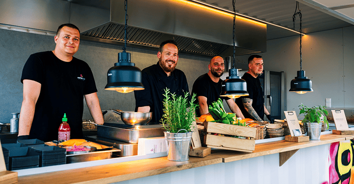 Vierköpfiges Kochteam bereitet gemeinsam Speisen im Foodtruck für das Messe-Catering zu.