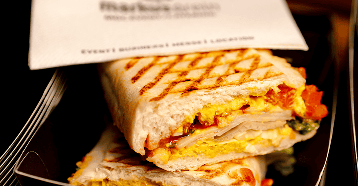 Gegrillte Panini-Sandwiches gestapelt neben einer Serviette mit Firmenlogo.
