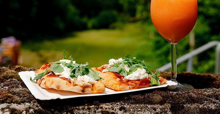 Pizza mit Rucola und ein Aperol Spritz auf einer Mauer mit grüner Landschaft im Hintergrund