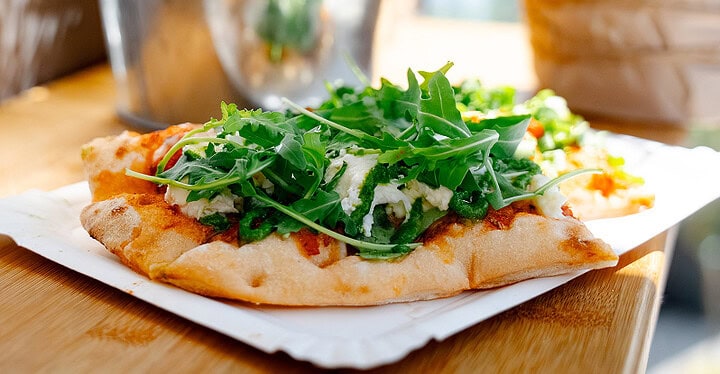 Stück Pizza mit Rucola und Mozzarella auf einem Pappteller beim Pizza Catering einer Hochzeit