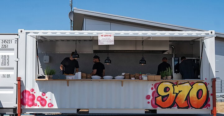 Weißer Foodtruck Container mit buntem 970 Graffiti und geöffneter Klappe unter blauem Himmel