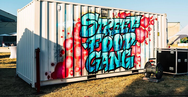 Weißer Foodtruck Container der Streetfood Gang mit buntem Graffiti steht im Freien auf einer grünen Wiese