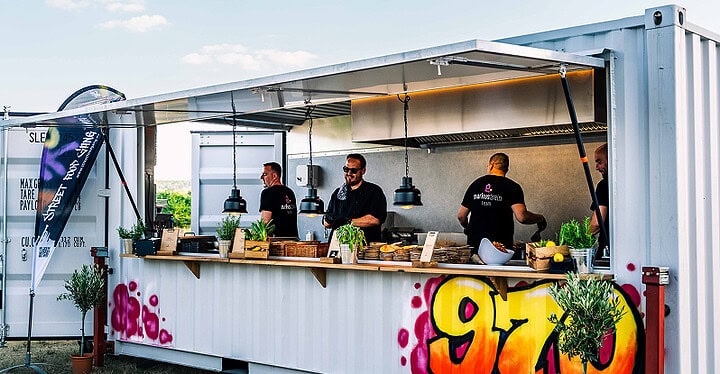 Geöffneter Container beim Foodtruck Catering mit Team bei der Zubereitung auf einem Event im Freien
