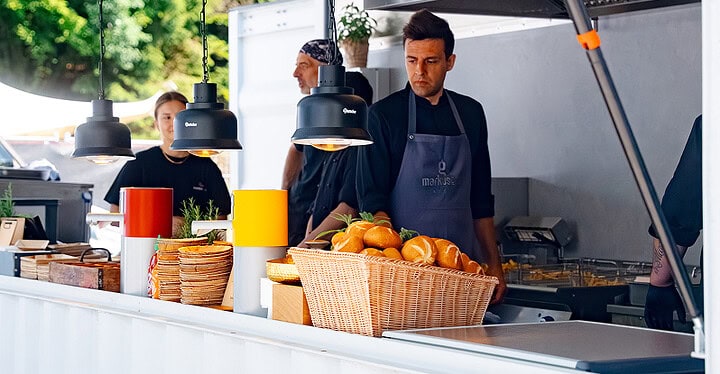 Koch an der Ausgabe beim Foodtruck Catering mit Körben voller frischer Brötchen