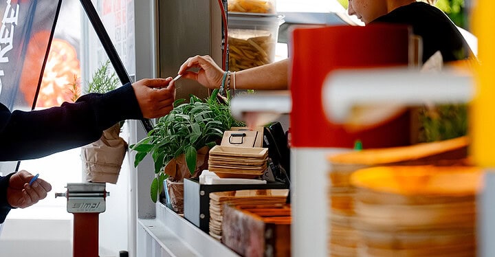 Gast bezahlt Essen am Tresen beim Streetfood Catering mit gestapelten Essensschälchen
