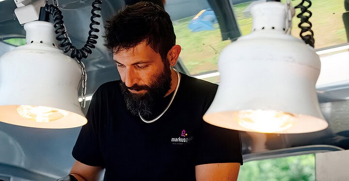 Koch von Markus Grein Catering bereitet im Foodtruck frische Gerichte unter Wärmelampen zu