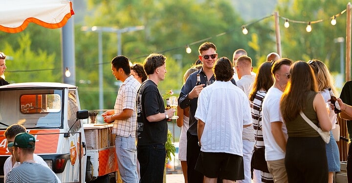 Viele Gäste stehen beim Event vamos. x Aperol am Maschinenhaus in Würzburg vor einer Ape als mobiler Aperol-Bar.