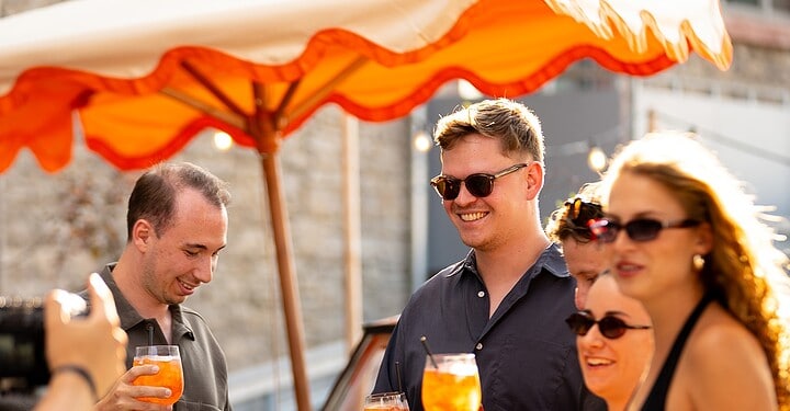 Beim DJ-Event von vamos. und Aperol am Maschinenhaus in Würzburg halten mehrere Gäste ein Glas Aperol Spritz in den Händen.