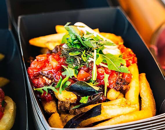 Vegane Loaded Fries mit Tomatensalsa und frischem Rucola in einer schwarzen Servierbox als Fingerfood