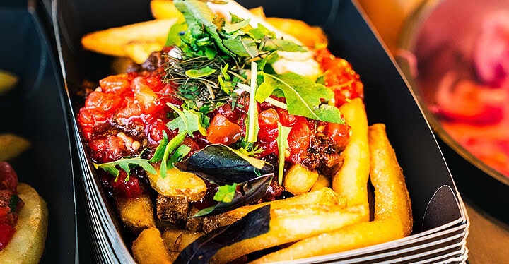 Vegane Loaded Fries mit Tomatensalsa und frischem Rucola in einer schwarzen Servierbox als Fingerfood