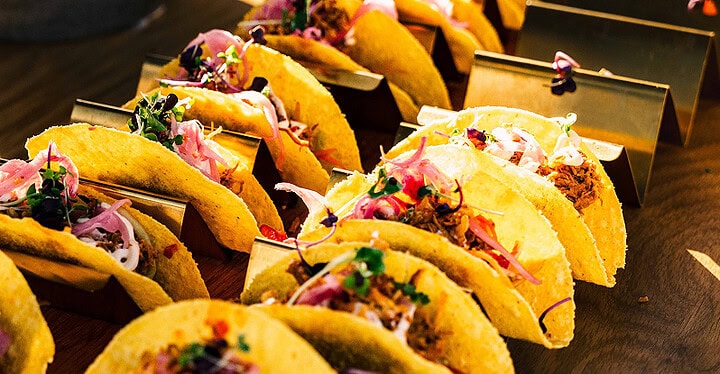 Aufgereihte bunte Tacos mit Gemüse, roten Zwiebeln und Kräutern auf einem vegetarischen Catering-Buffet