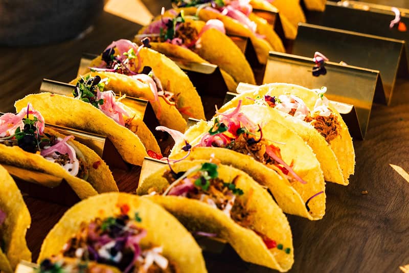 Aufgereihte bunte Tacos mit Gemüse, roten Zwiebeln und Kräutern auf einem vegetarischen Catering-Buffet